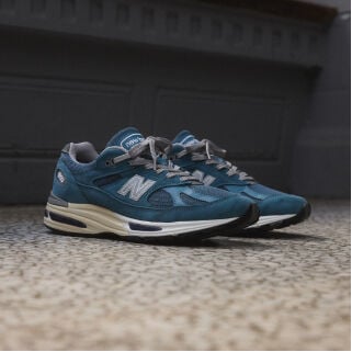 A pair of New Balance Made in UK sneakers sitting on a concrete floor.