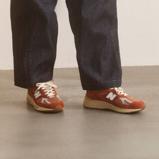 A pair of New Balance Made in UK sneakers in front of a rabbit in a brown textured studio environment. 