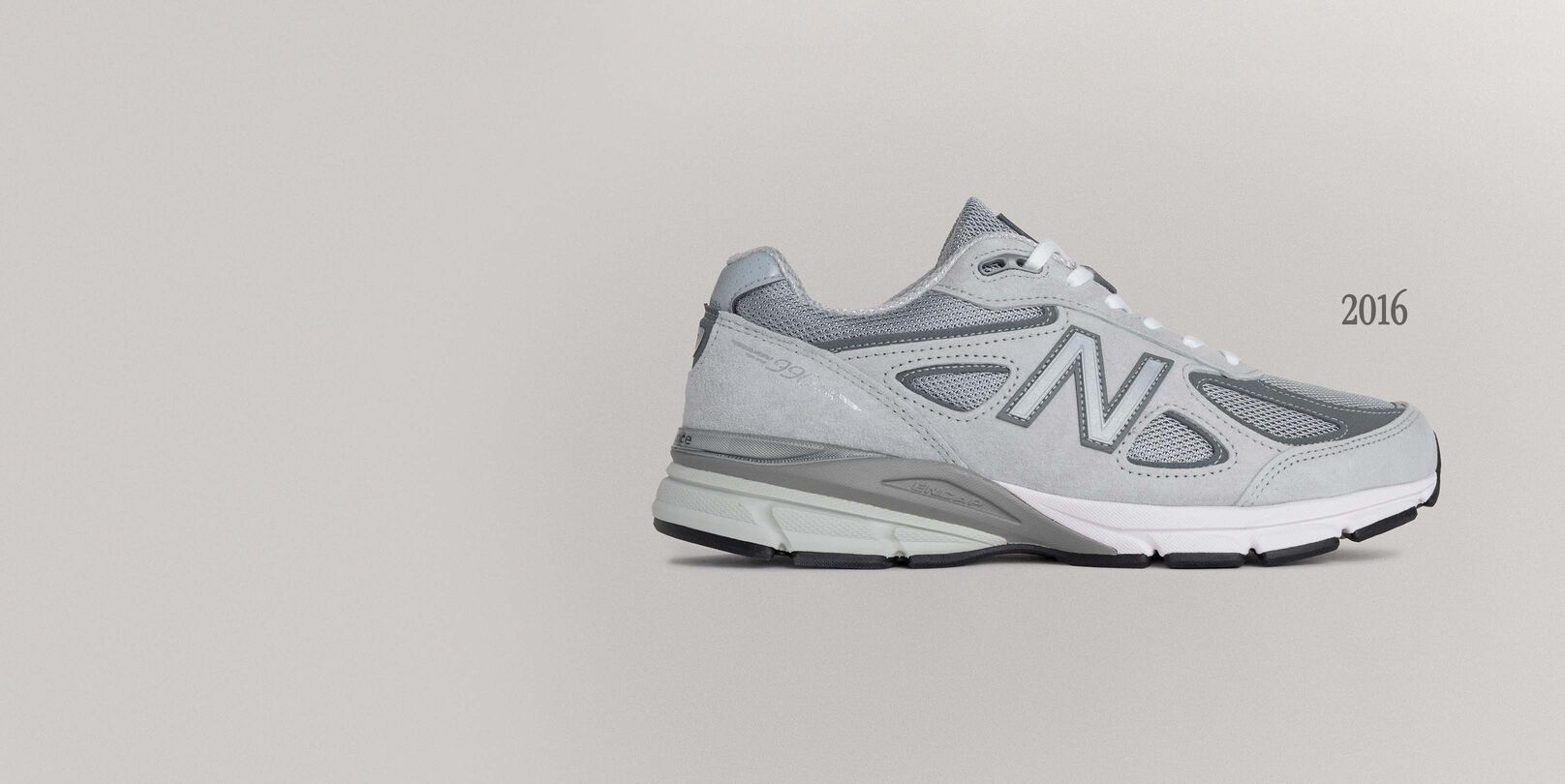 A grey 990v4 sneaker sitting on a grey background.
