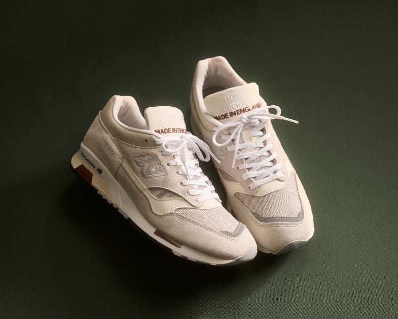 A pair of New Balance Made in UK sneakers on a green textured studio environment. 