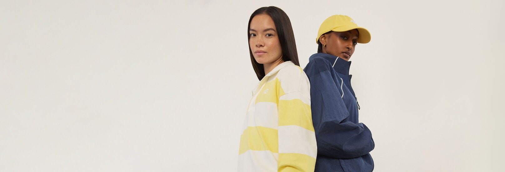 Two woman wearing New Balance standing back to back and looking at the viewer.