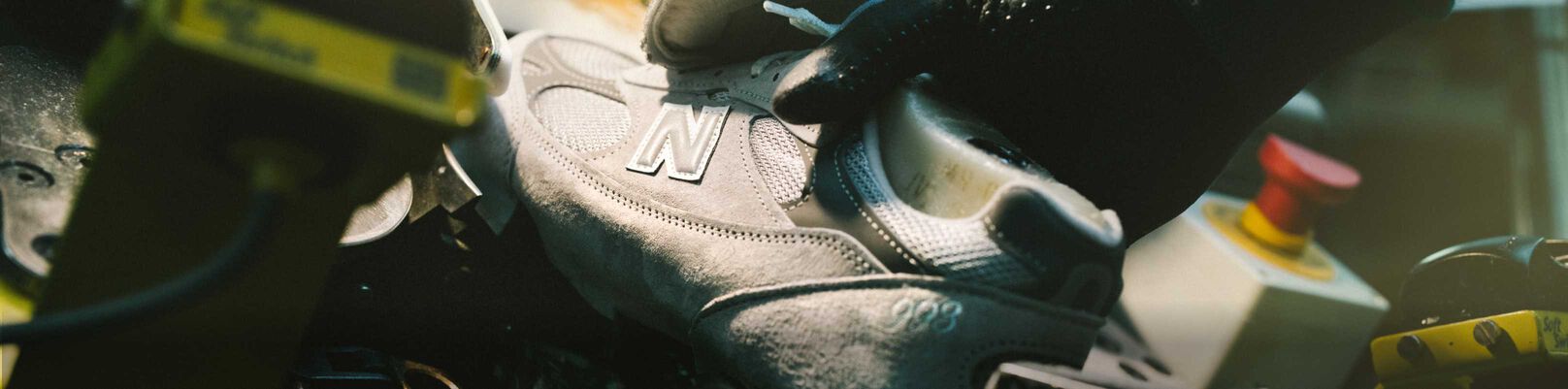 A hand putting a New Balance shoe in a device in a factory environment.