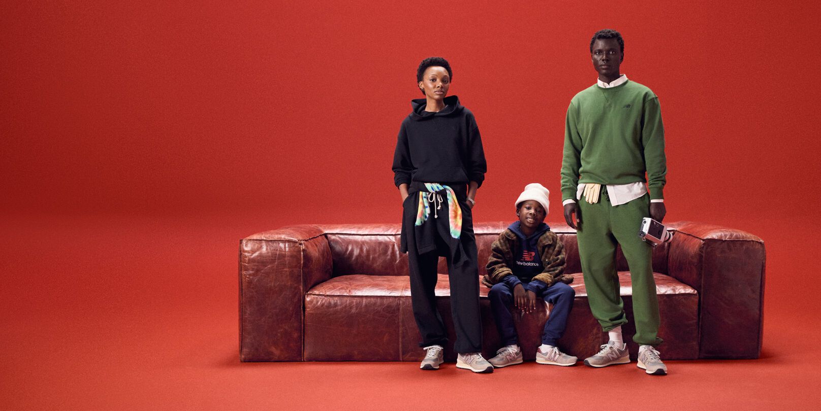 A group of people wearing New Balance standing next to a sofa with a red background.